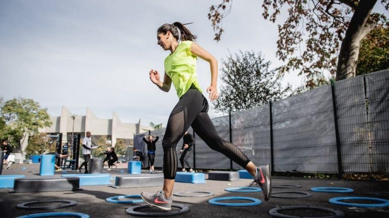 woman in green tank top and black leggings doing yoga on blue round trampoline